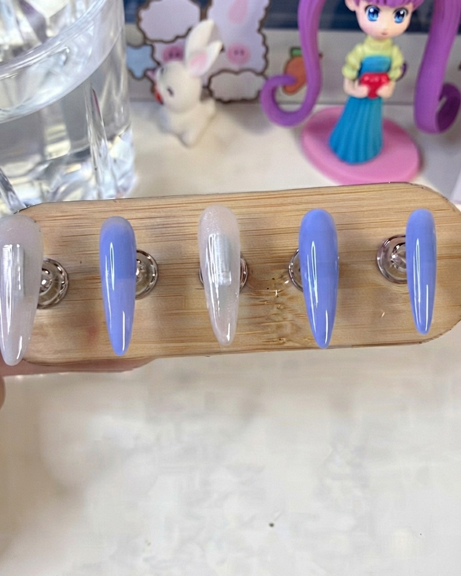 Un supporto per unghie che mostra unghie dipinte di blu e bianco latte mentre polimerizzano sotto una lampada UV/LED.