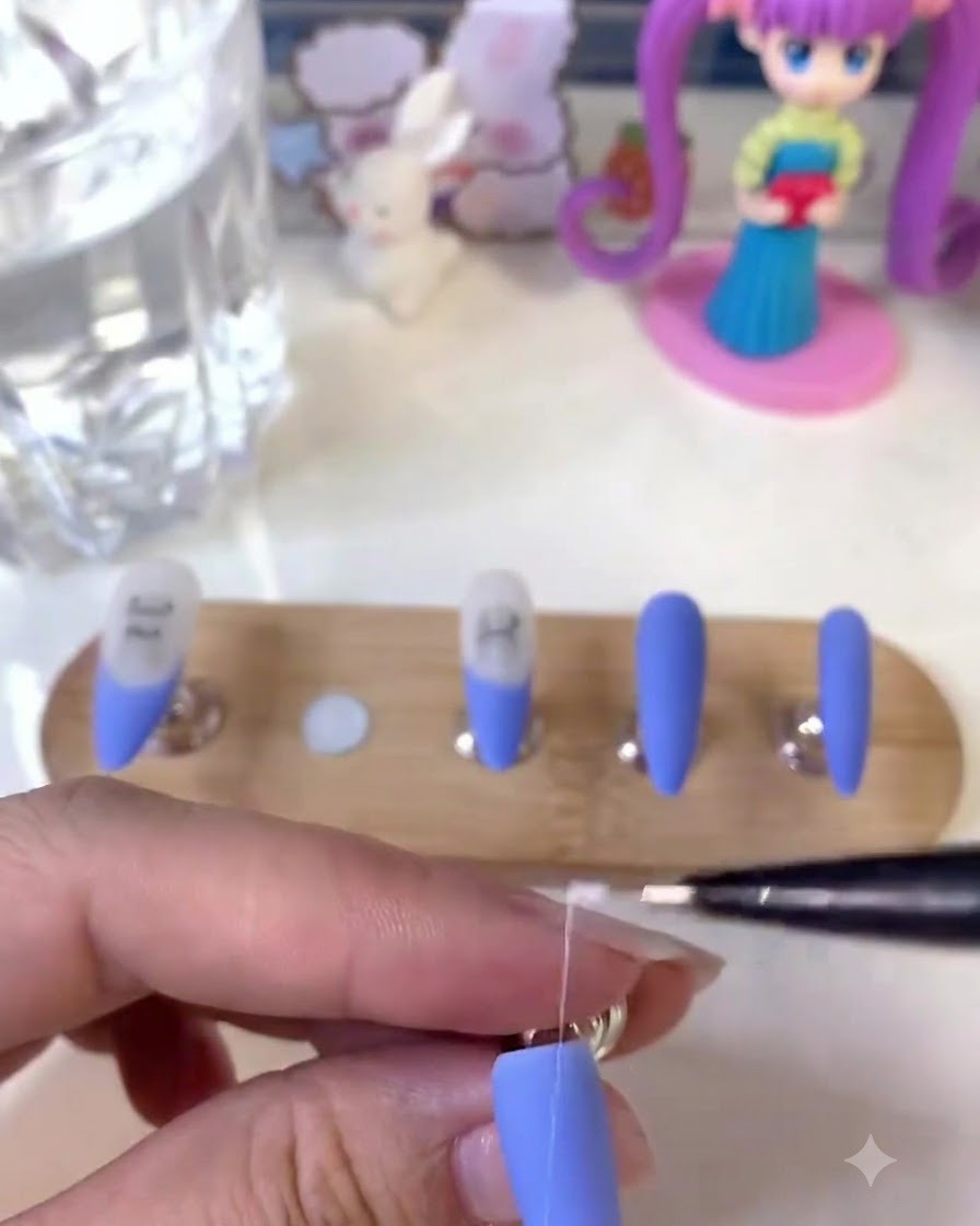 Unonicotecnica che tiene un pennello liner fine e disegna dettagliate linee bianche su ununghia blu opaca.