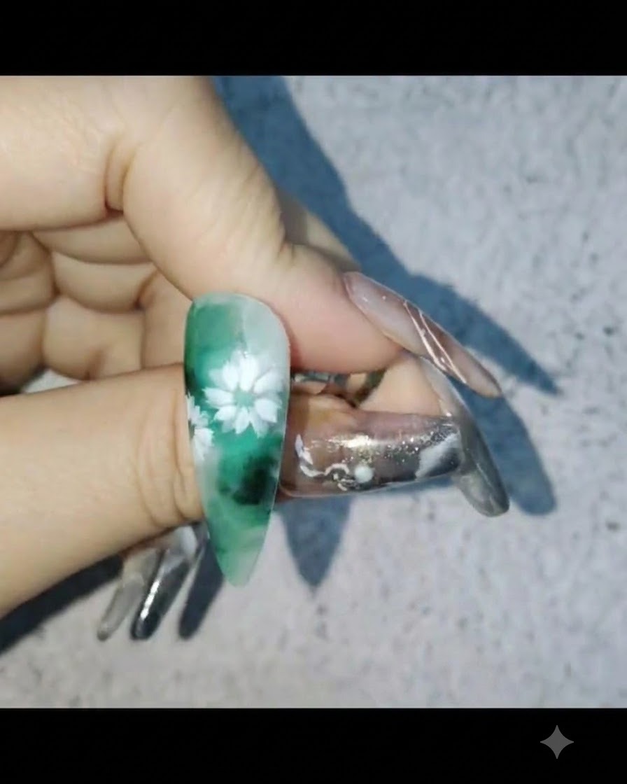 Una mano che tiene ununghia con nail art di margherite bianche mentre applica uno strato protettivo di gel rinforzante.