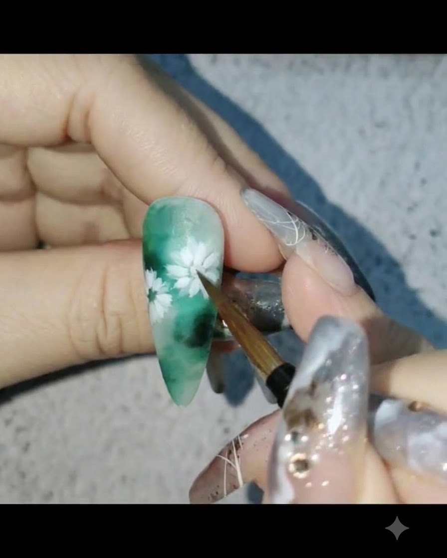 Un pennello per unghie che applica il top coat opaco su un design floreale a tema verde.