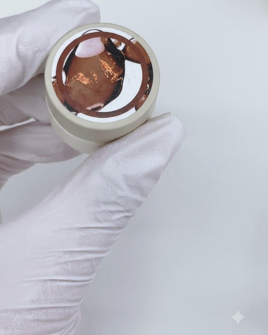 Un pennello piatto applica uno strato di smalto gel marrone trasparente su ununghia finta per esposizione.