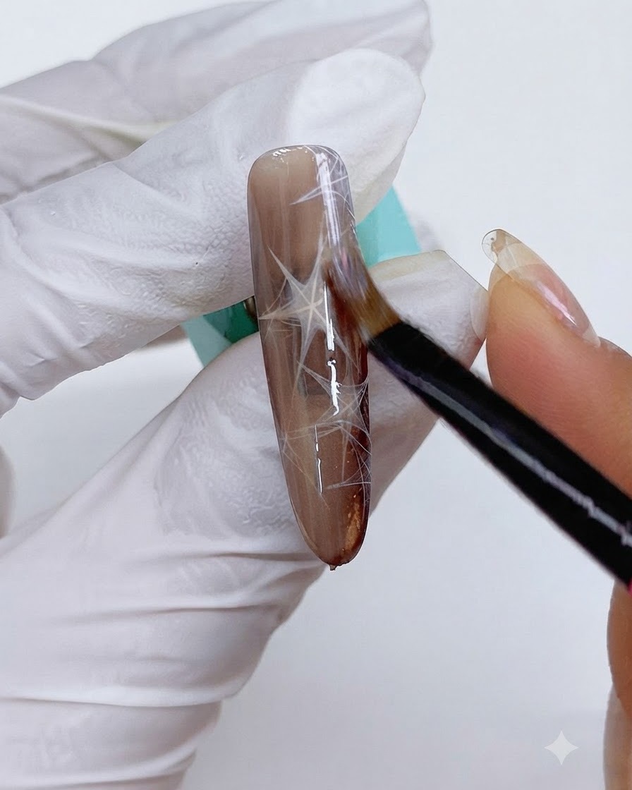 Un pennello sottile che applica il gel cat eye sullunghia marrone decorata.