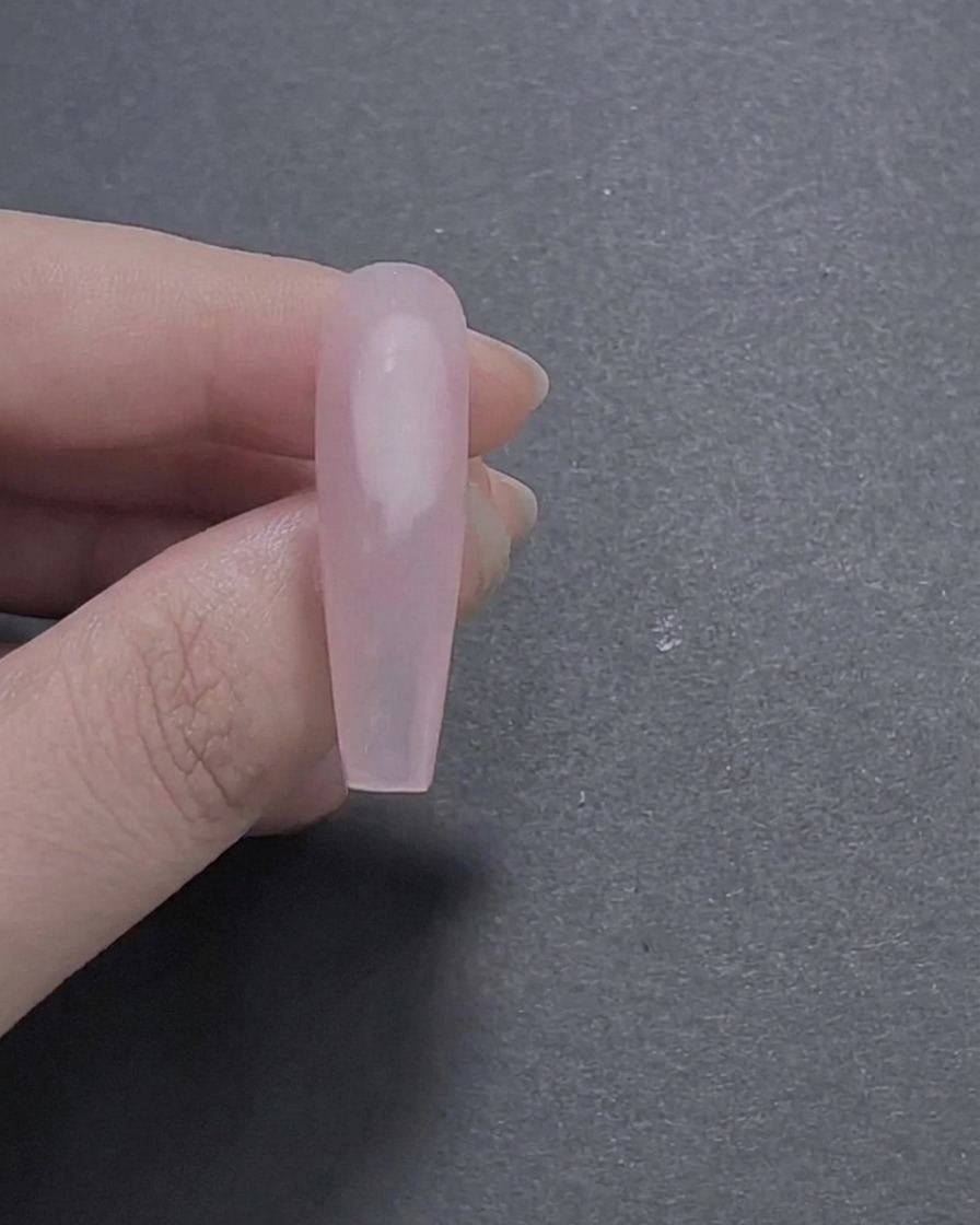 Un primo piano di ununghia lunga a forma di cofano dipinta con una base in gel rosa trasparente liscia e lucida tenuta tra le dita.