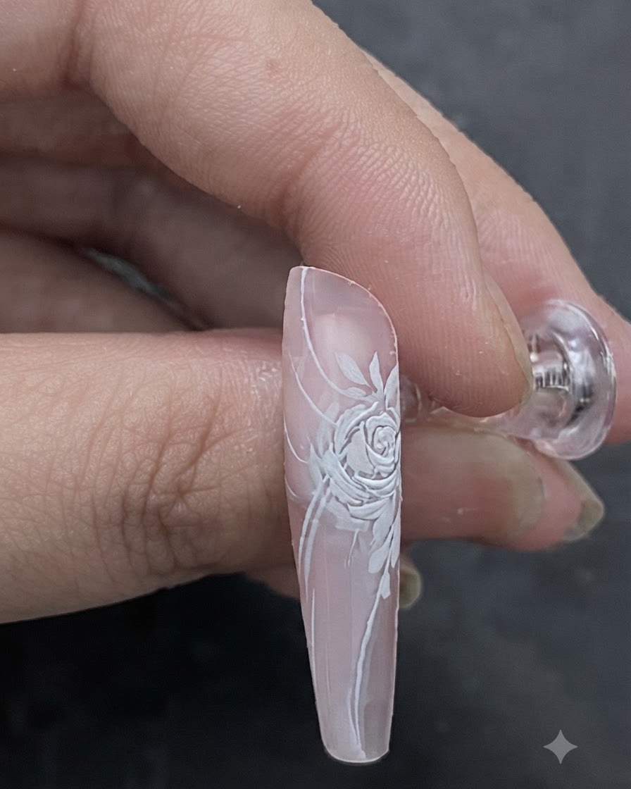 Unimmagine in primo piano che mostra una tonalità di rosa chiaro applicata a pennello al centro di un design di unghia con rosa bianca dimensionale.
