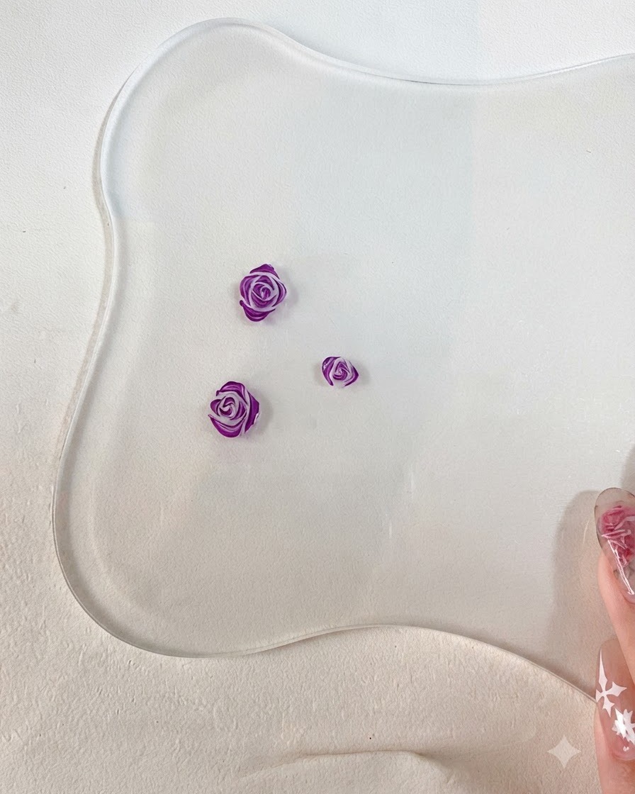 Un primo piano di un pennello per nail art fine che aggiunge dettagliati contorni viola scuro ai bordi dei petali di rosa 3D scolpiti.