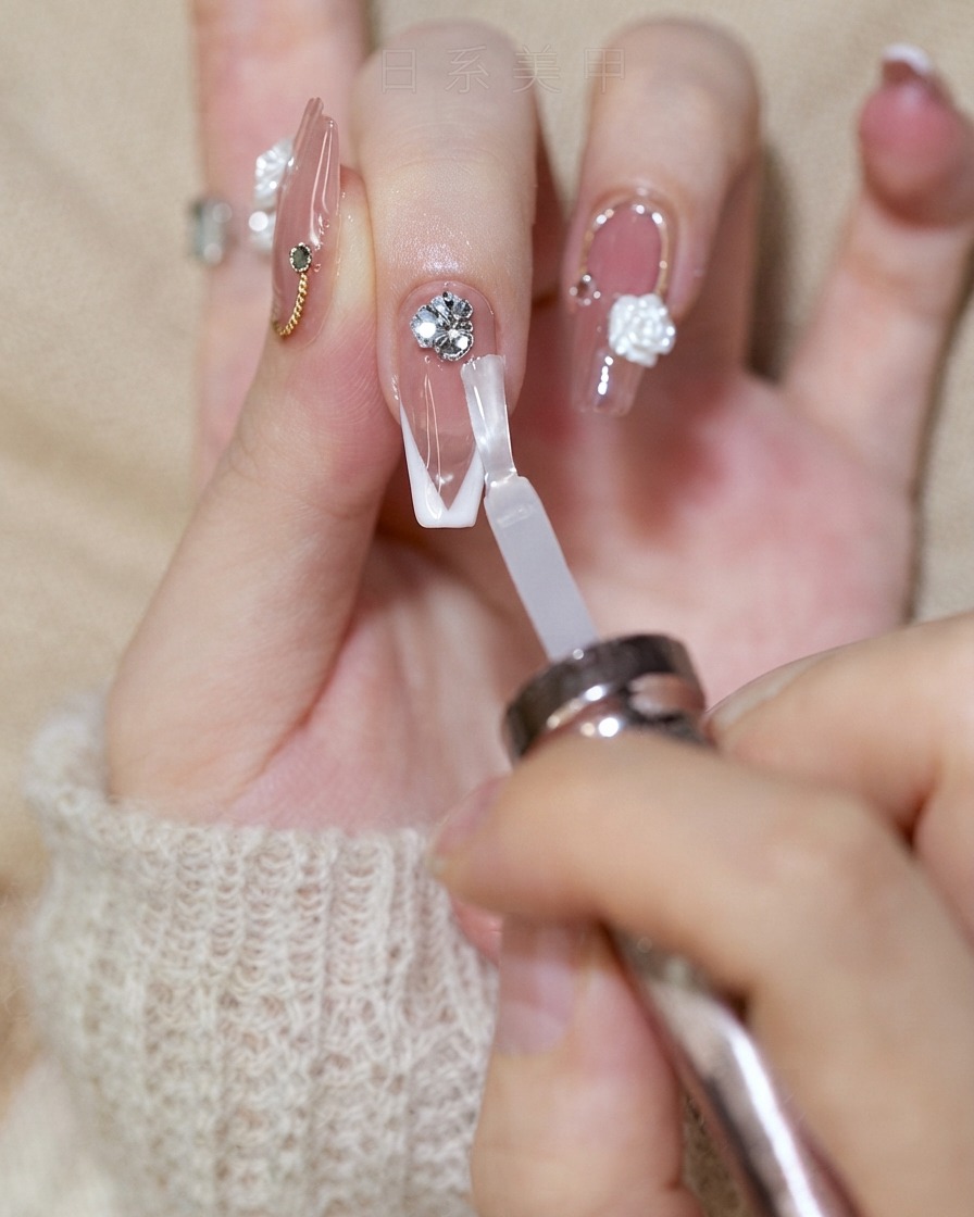 Un pinceau à ongle appliquant un top coat brillant sur un ongle à french tip tout en contournant le groupe de strass.