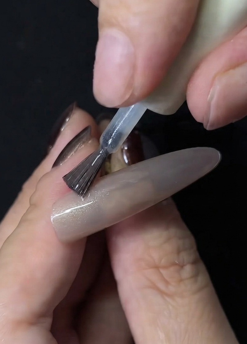 Un pennello per unghie che applica smalto gel cat eye trasparente sulla superficie di unextension per unghie nude.