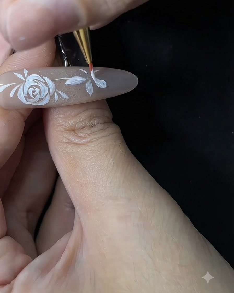 Unonicotecnica che utilizza un pennello sottile per rifinire e ispessire i petali bianchi di un piccolo fiore su unextension per unghie in gel.