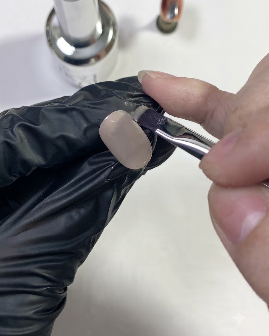 Una mano guantata che stende un colore di base nude su una tip di unghia.