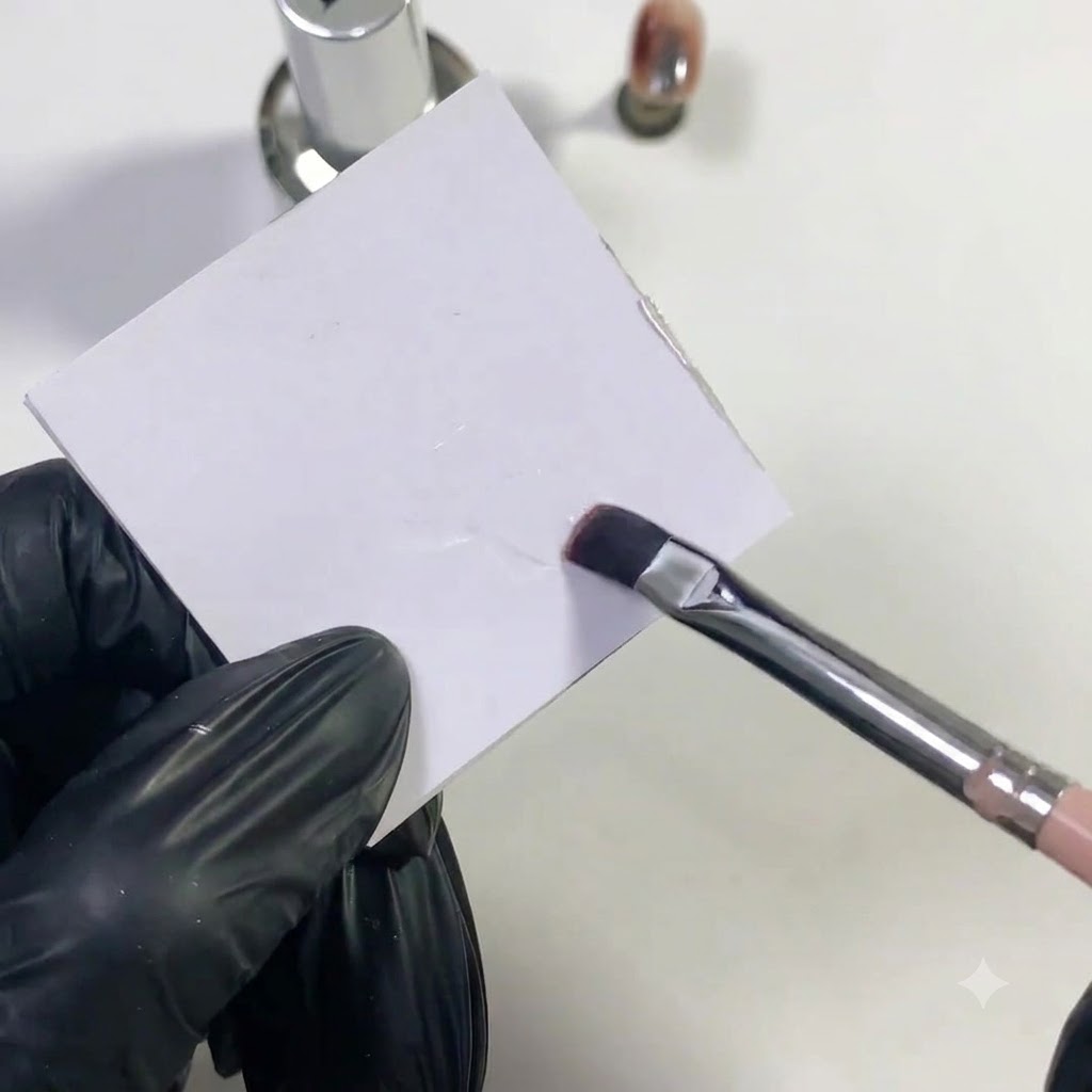 Un pennello per unghie piatto che tampona del base gel chiaro su una superficie di plastica bianca.
