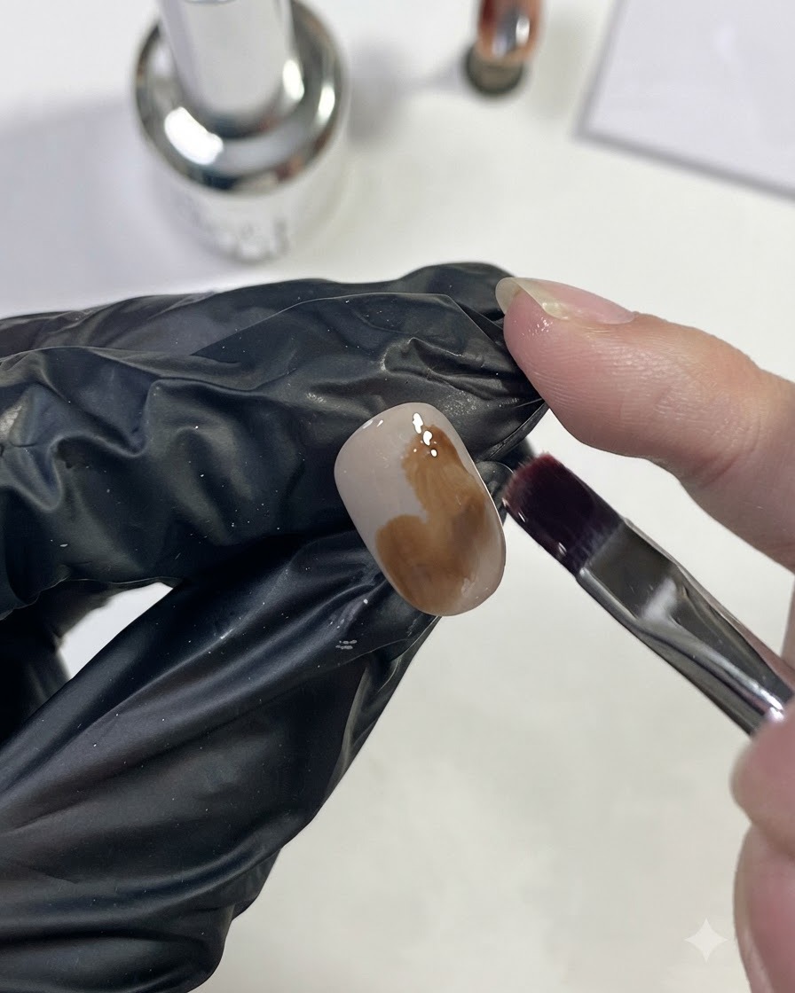 Un pennello per unghie che applica del gel marrone caramello chiaro in una grande chiazza sullunghia.