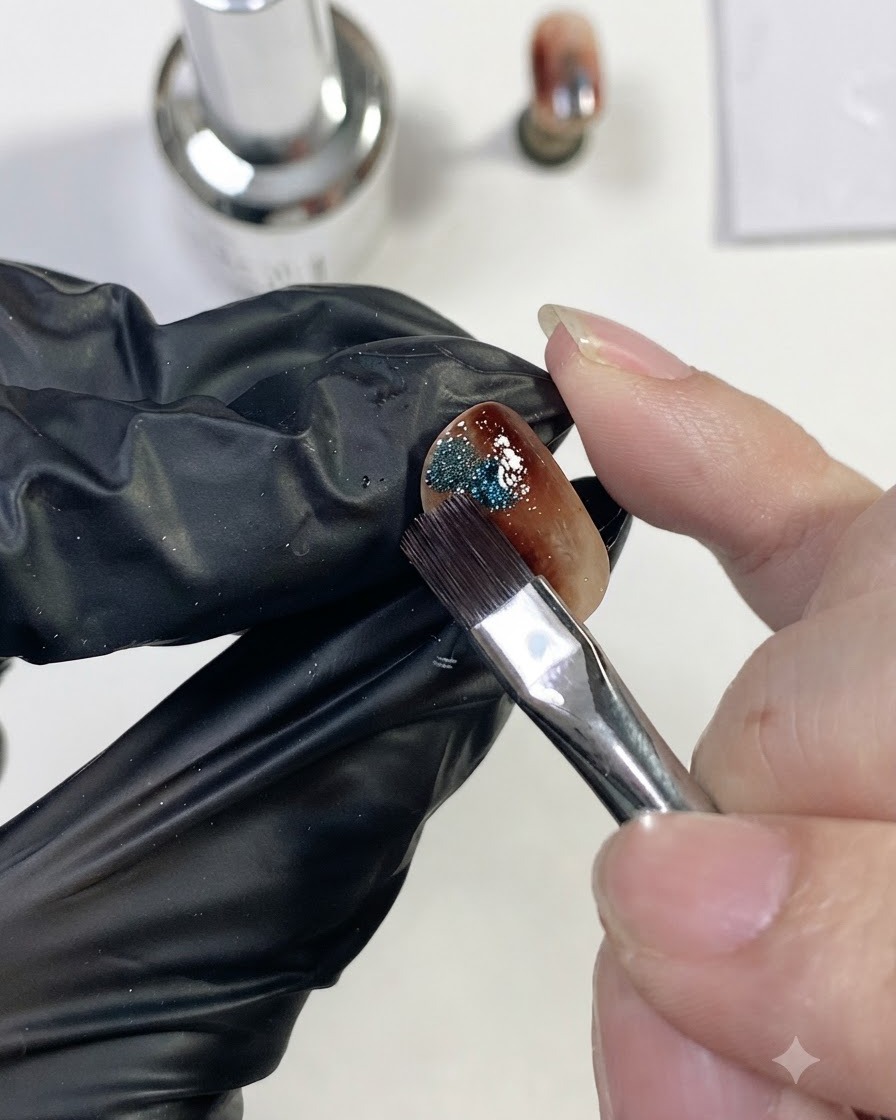 Un pennello per unghie che posiziona una piccola goccia di gel cat-eye magnetico blu brillante sul lato dellunghia ambra.