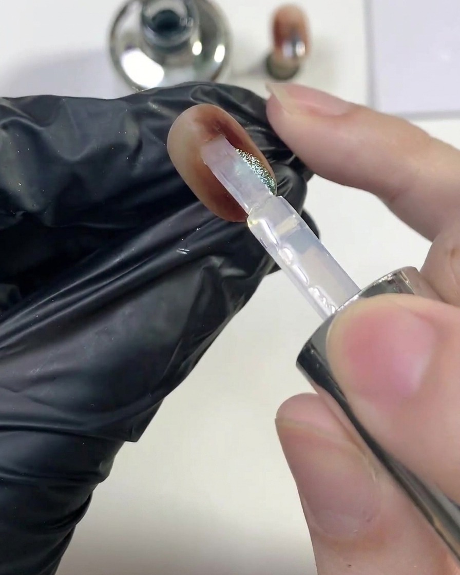 Un pennello che fa scivolare uno strato generoso di top coat trasparente lucido sopra lunghia finita ambra cat-eye.
