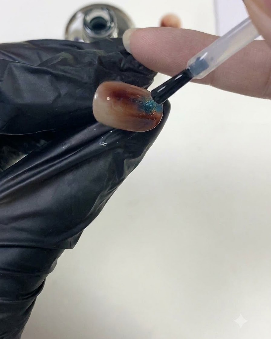 Un pennello per unghie che leviga il top coat trasparente sopra una superficie di unghia ambra testurizzata per costruire lapice.