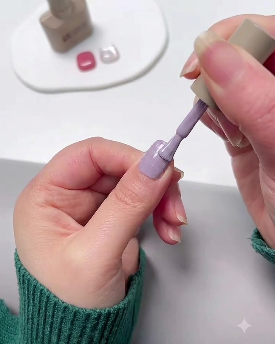 Un pennello da unghie applica lo smalto gel viola lavanda su ununghia.