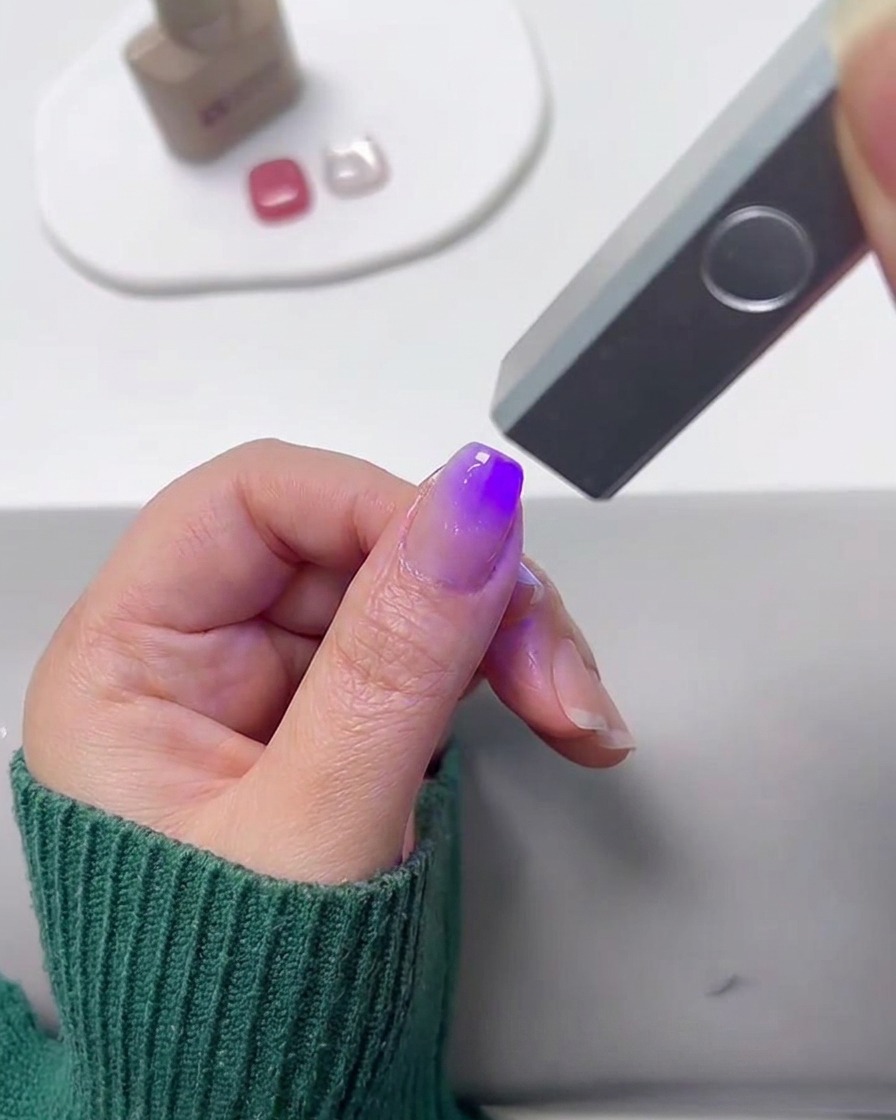 Una mini lampada UV polimerizza ununghia dipinta con la sfumatura.