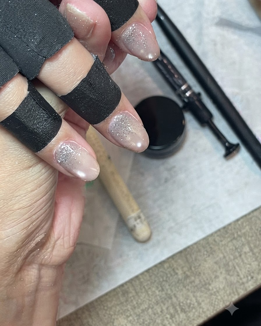Una mano che indossa protezioni nere per le dita utilizza un pennello liner fine per sfumare e distribuire il gel glitter lungo lunghia.
