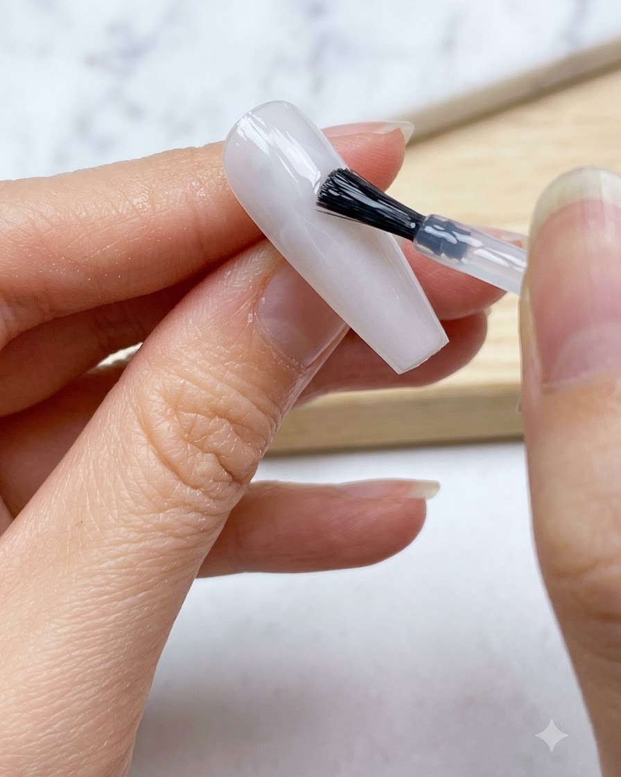 Un pennello per unghie applica uno strato uniforme di base in gel bianco lattiginoso traslucido su tutta lunghia.