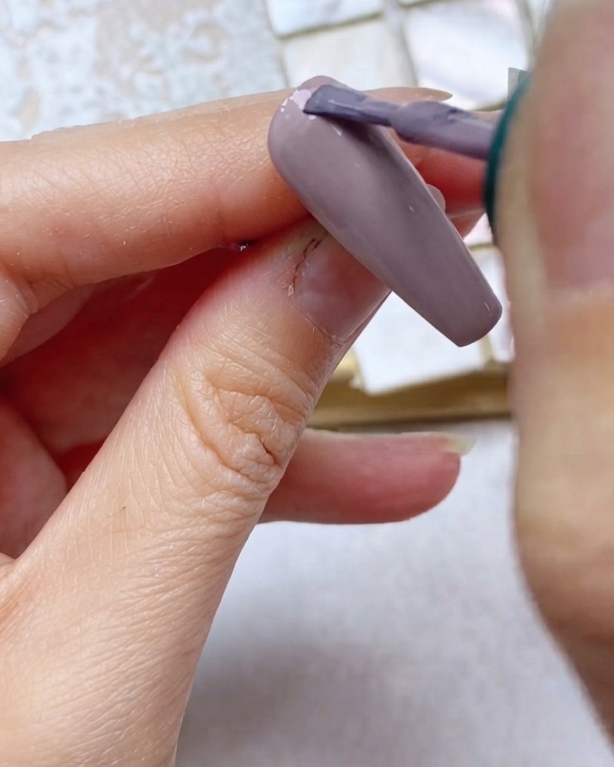 Un pennello applica lo smalto gel grigio-viola sul terzo superiore dellunghia vicino alla cuticola.