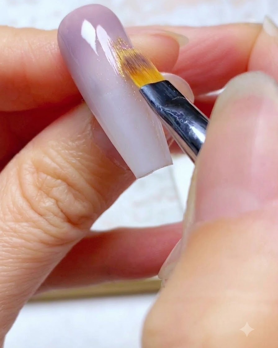 Un pennello ombré sfuma il secondo strato di gel viola verso il basso sullunghia.