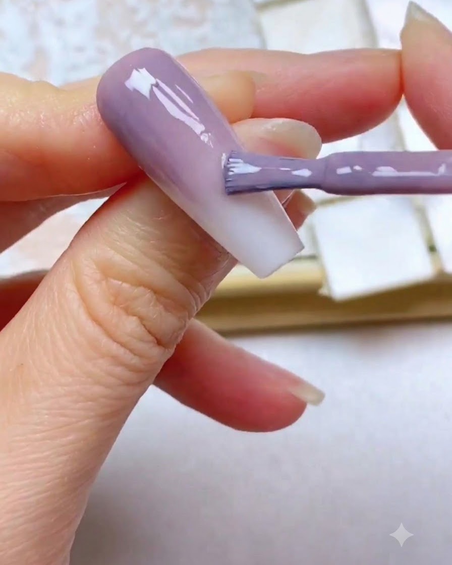 Un pennello per gel applica un terzo strato di colore viola vicino al bordo superiore dellunghia.