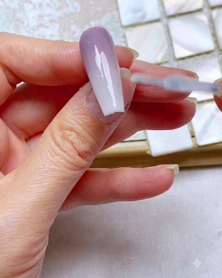 Un pennello per top coat scorre fluidamente su ununghia rifinita con gradiente bicolore per sigillare e aggiungere lucentezza.