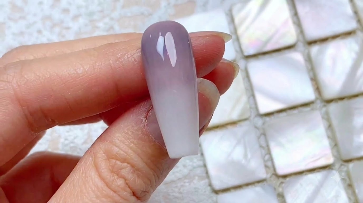 Primo piano di ununghia completata con gradiente verticale bicolore, che sfuma da un grigio-viola polveroso nella zona cuticola a un bianco lattiginoso sulla punta.