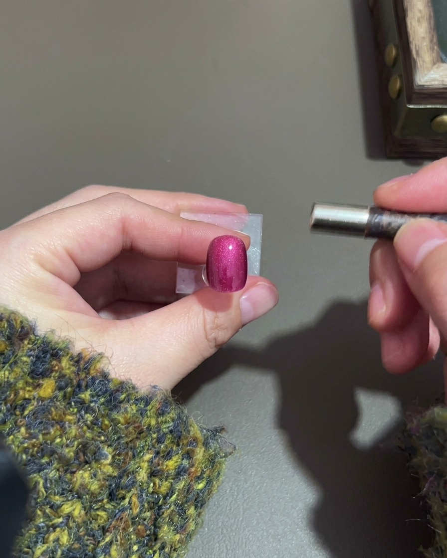 Una mano che tiene un magnete accanto a ununghia cat-eye viola scuro per formare un punto luce.
