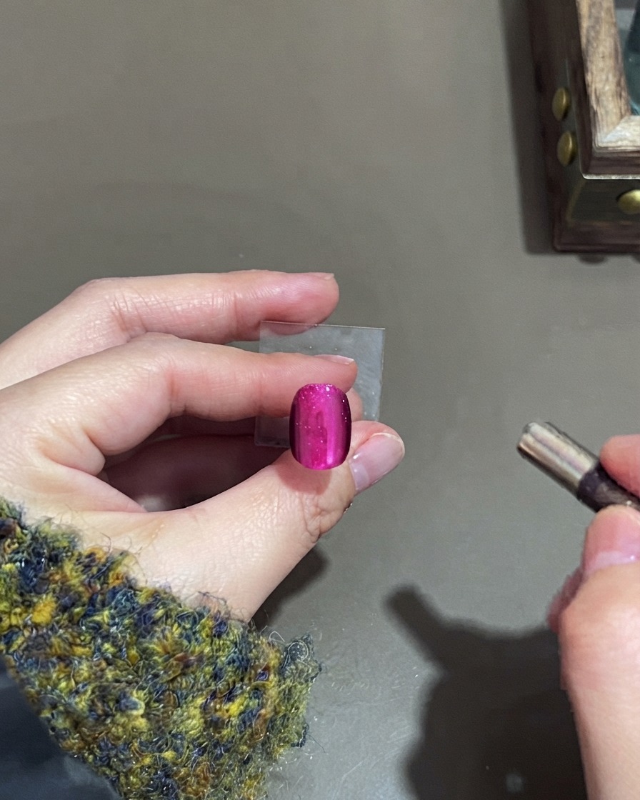 Un piccolo magnete cilindrico vicino a ununghia in gel cat-eye rosa per modellare il punto luce.