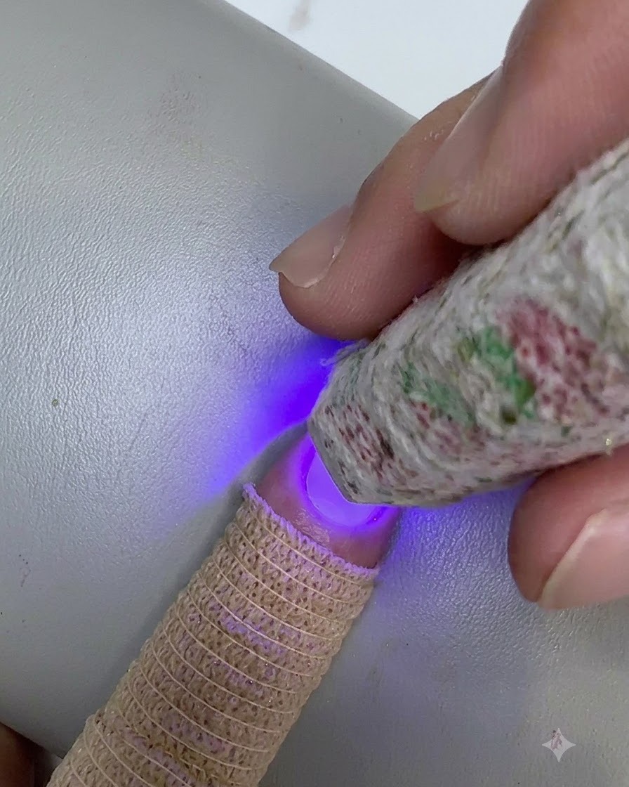Una mini lampada UV/LED decorata tenuta sopra la punta di ununghia mentre polimerizza uno strato sfumato di gel trasparente.