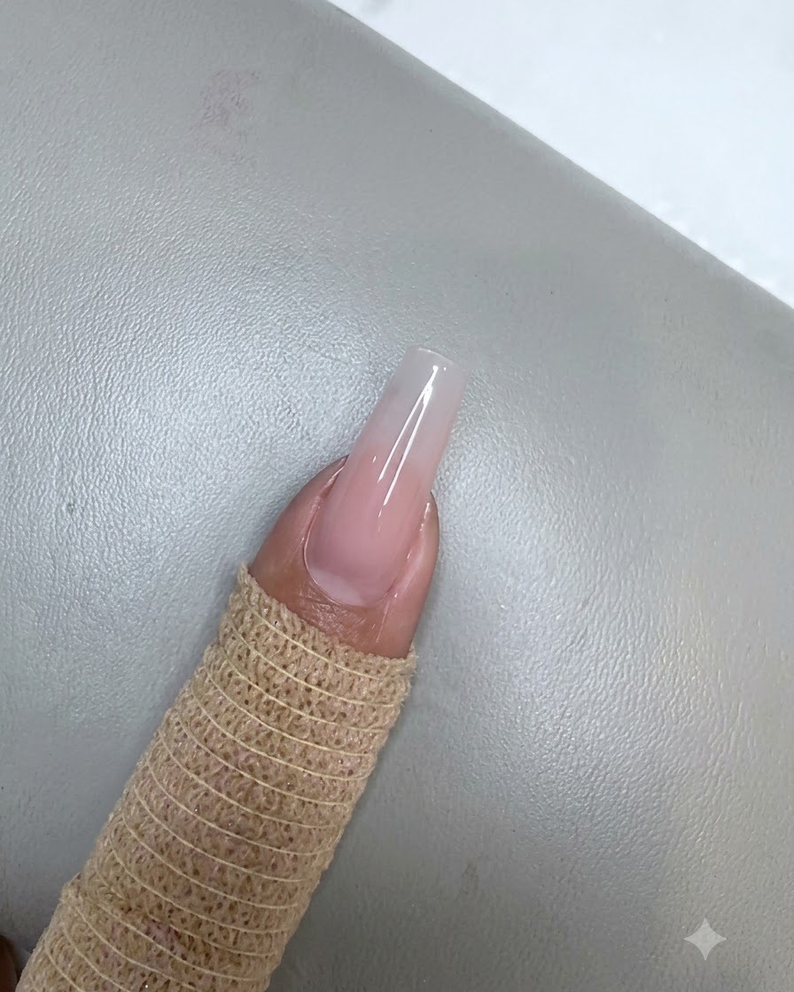 Ununghia con unapplicazione di gel rosa nude polimerizzata posizionata sotto una piccola lampada UV LED viola.