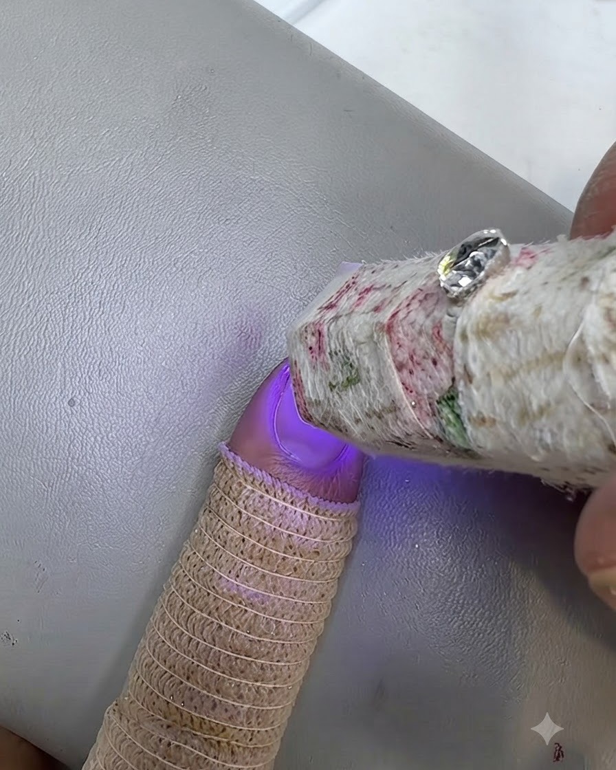 Una piccola lampada UV che polimerizza ununghia dipinta con un dito che indossa un copridito in maglia.