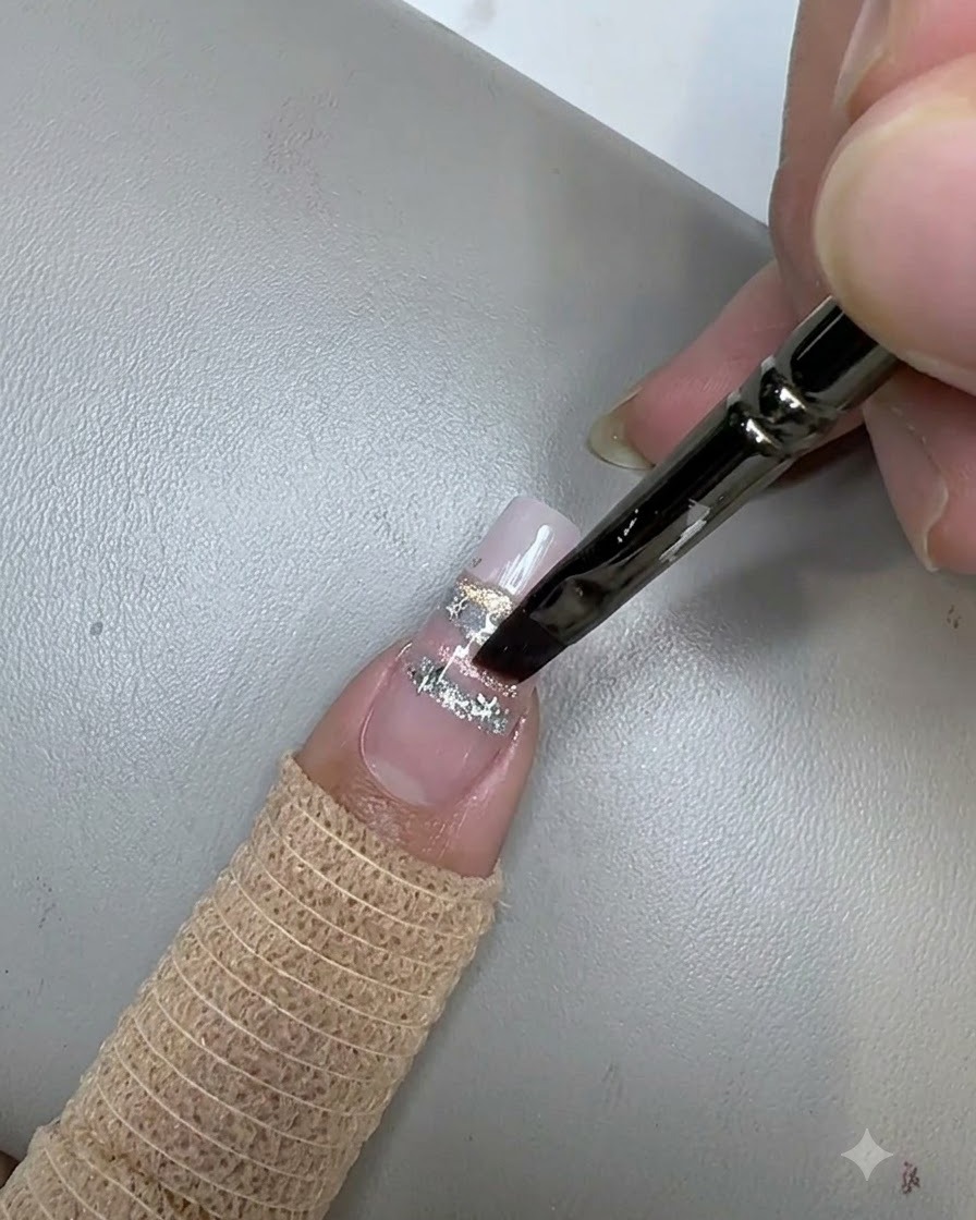 Un pennello per unghie che applica un top coat trasparente sopra le paillettes a stella su ununghia decorata.