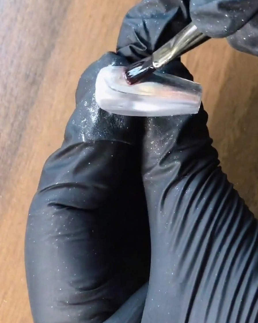 Un pennello applica il gel di rinforzo trasparente su ununghia in cromo argento.