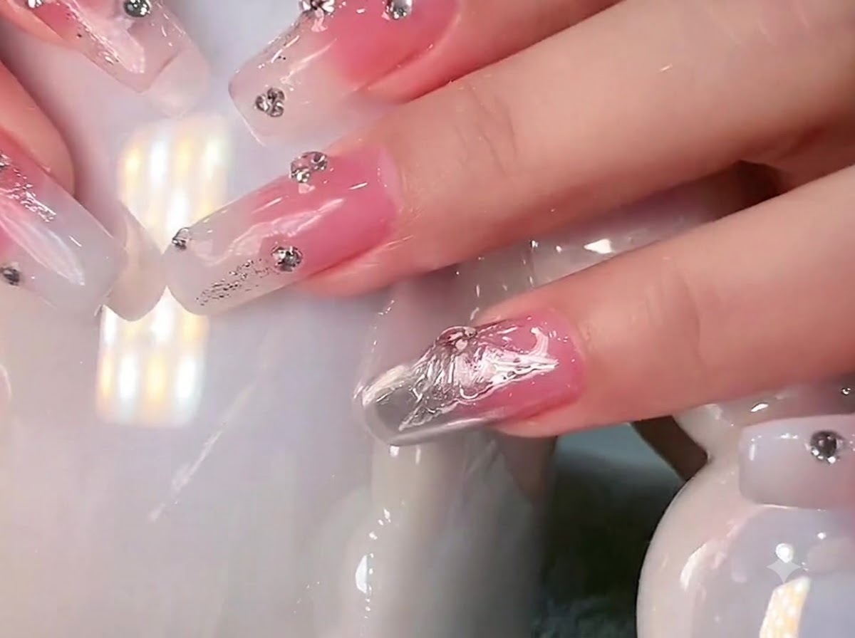 Primo piano di unghie lunghe quadrate con sfumatura bianco latte e strass tenute contro una tazza di ceramica bianca.