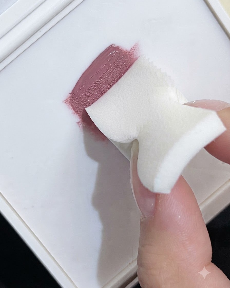 Una spugnetta da trucco che preleva smalto gel rosa da una tavolozza bianca per creare una texture sfumata.