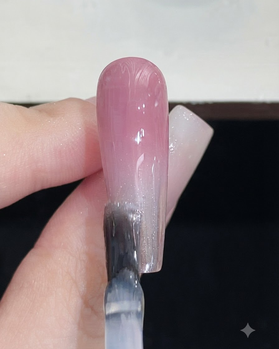 Un pennello per unghie che applica un top coat trasparente su ununghia finita con sfumatura rosa.