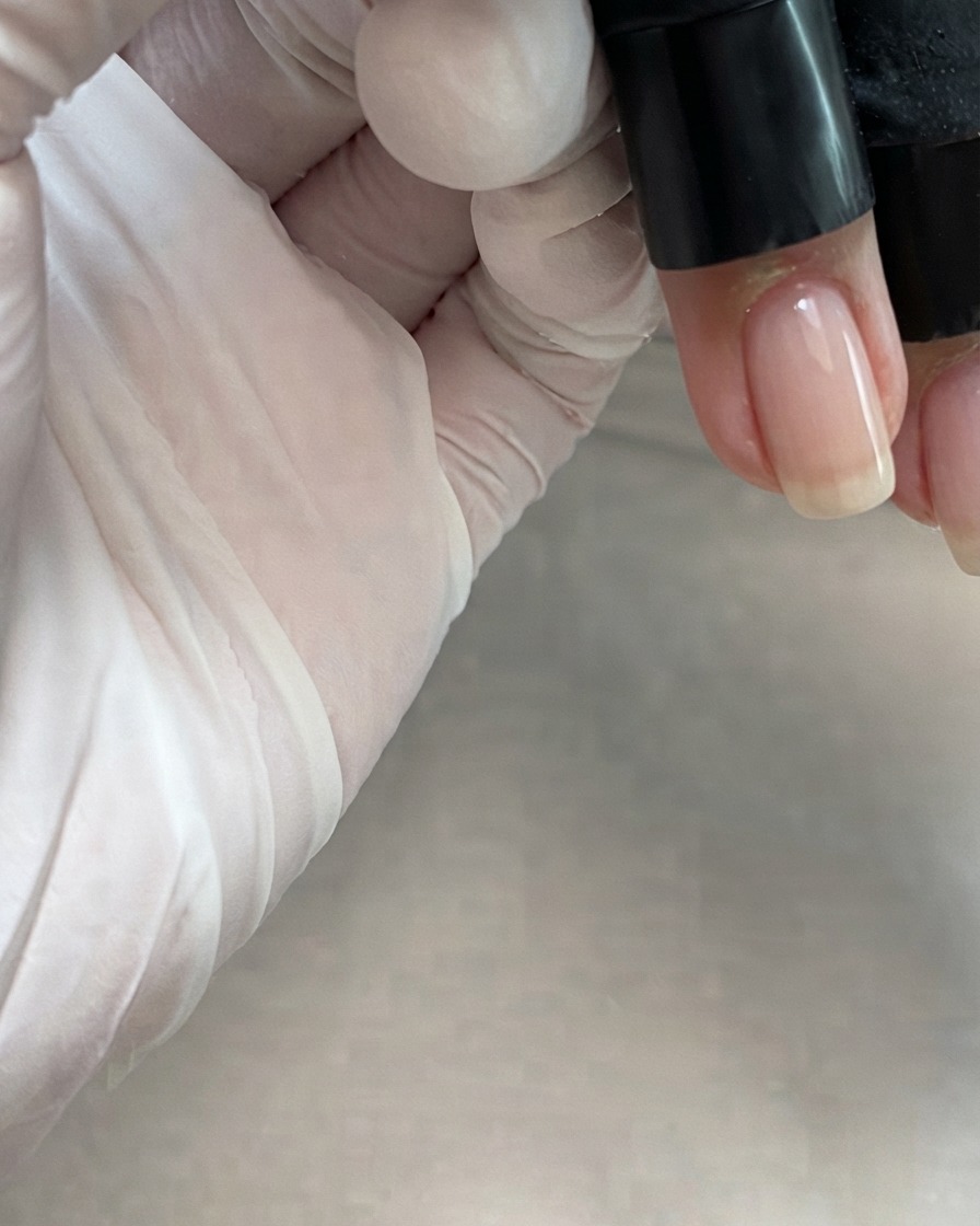 Pennello da boccetta che applica un gel rosa nude semitrasparente lungo il centro di ununghia.