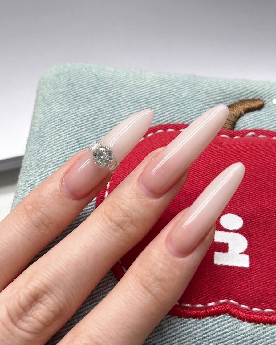 Primo piano di un pennello che applica del pigmento gel bianco sulla punta di una lunga unghia a stiletto color nude.