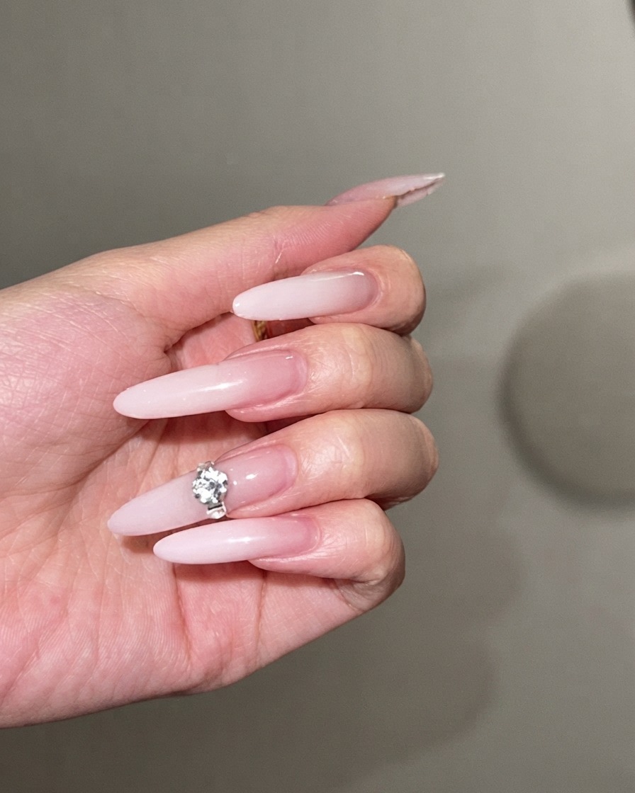 Un grande strass scintillante che viene premuto al centro di una lunga unghia a stiletto con sfumatura bianco latte.