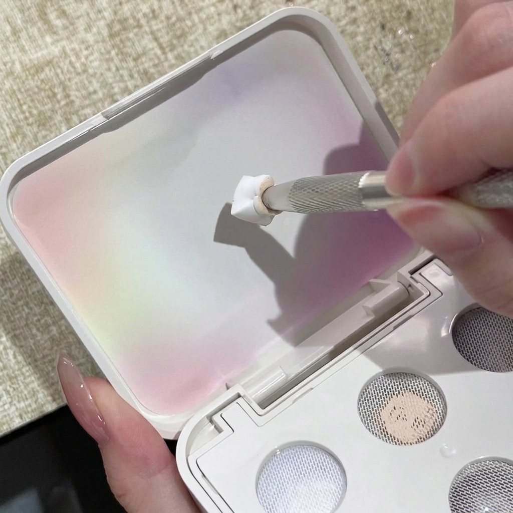 Uno strumento in metallo per unghie che preme il gel solido bianco sulla griglia ruvida del coperchio di una palette.