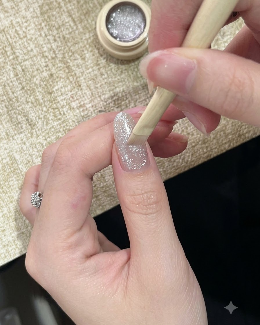 Un pennello che applica uno smalto gel cat-eye argento altamente riflettente e scintillante su ununghia.