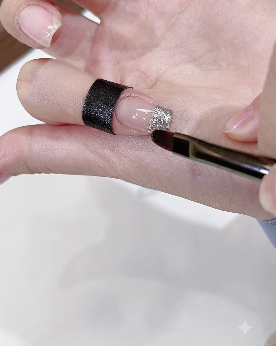 Un pennello piatto per nail art applica il gel con glitter argento sulla punta di ununghia nude.