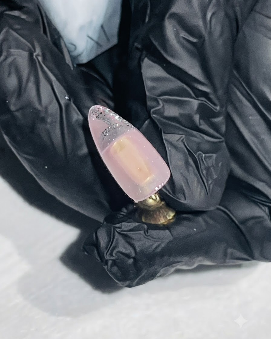 Un pennello liner sottile che disegna un contorno argento sulla punta di ununghia color nude.