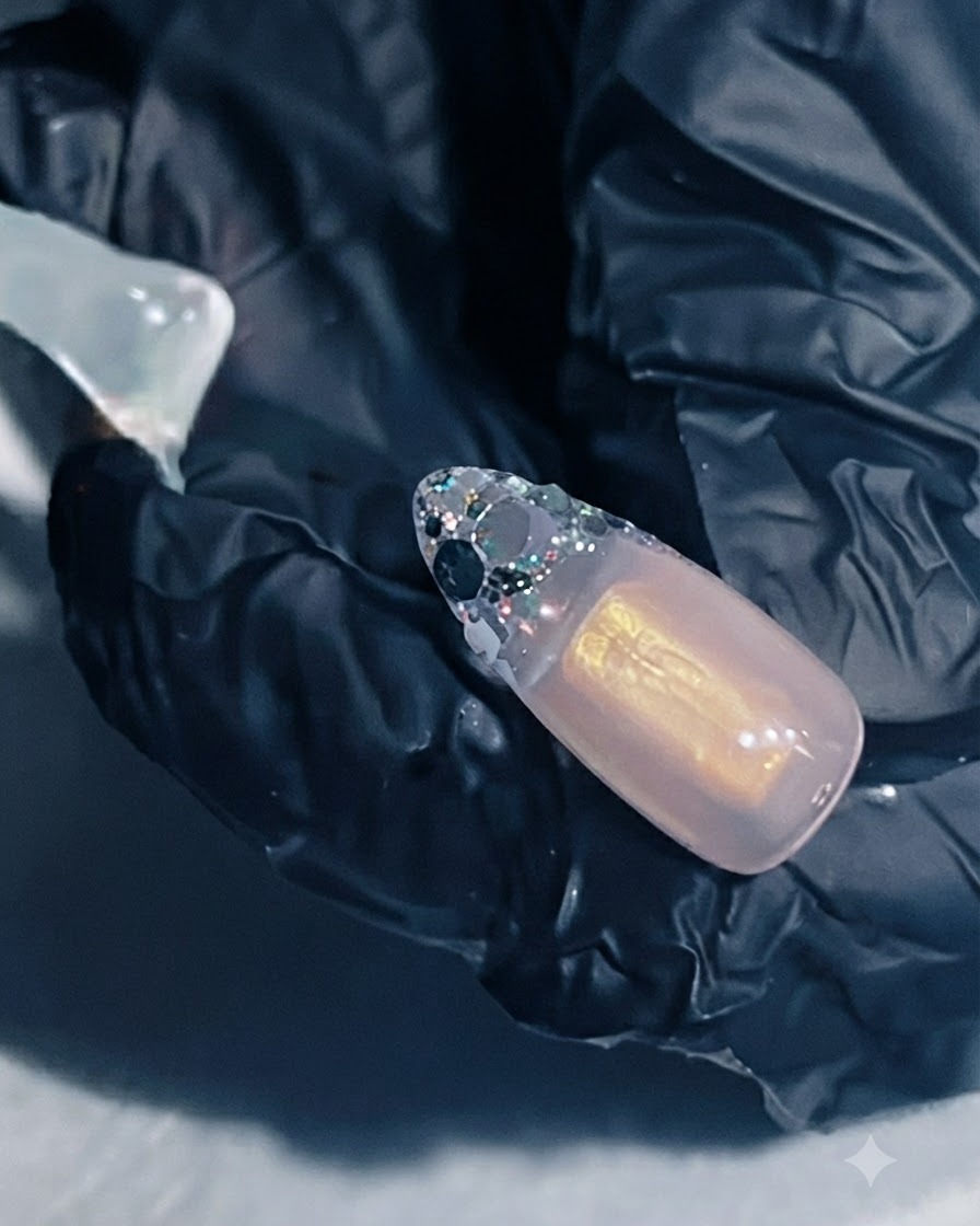 Una mano che tiene unestensione ungueale con gel rinforzante applicato sullarea della French con glitter.