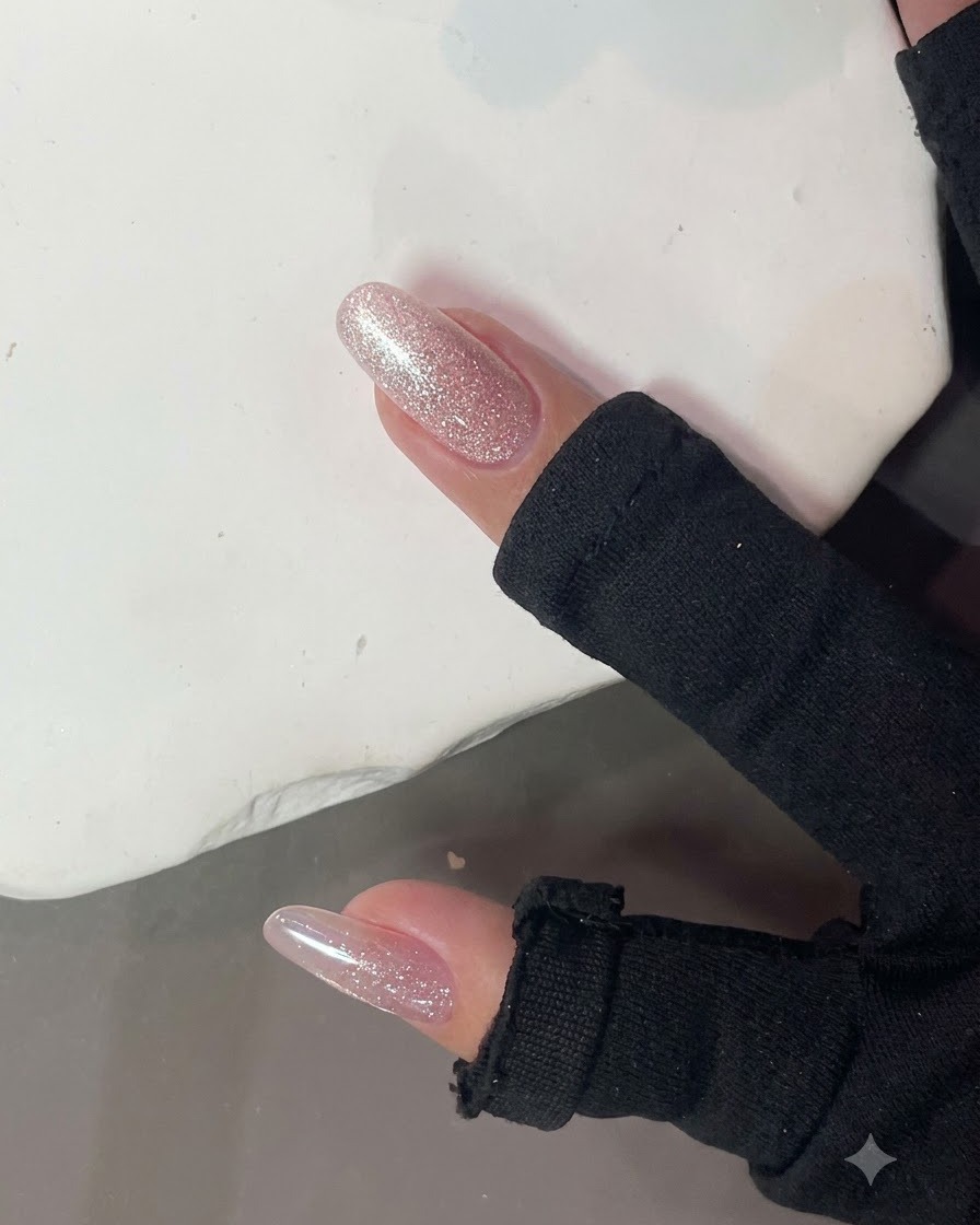 Un forte magnete per unghie tenuto vicino a ununghia glitterata rosa lucida per formare un effetto luce cat-eye.