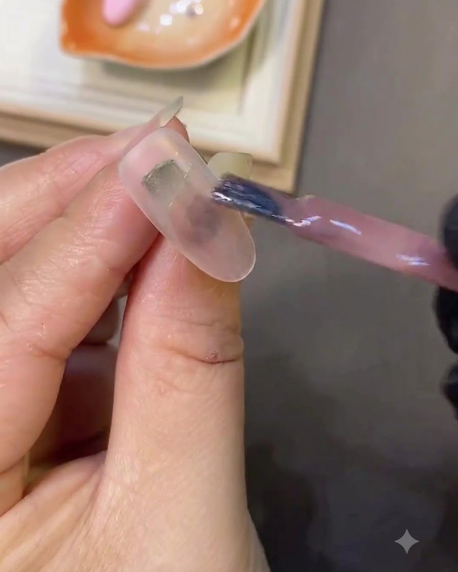 Un pennello da unghie che applica il gel cat-eye rosa chiaro su ununghia bianca latte.
