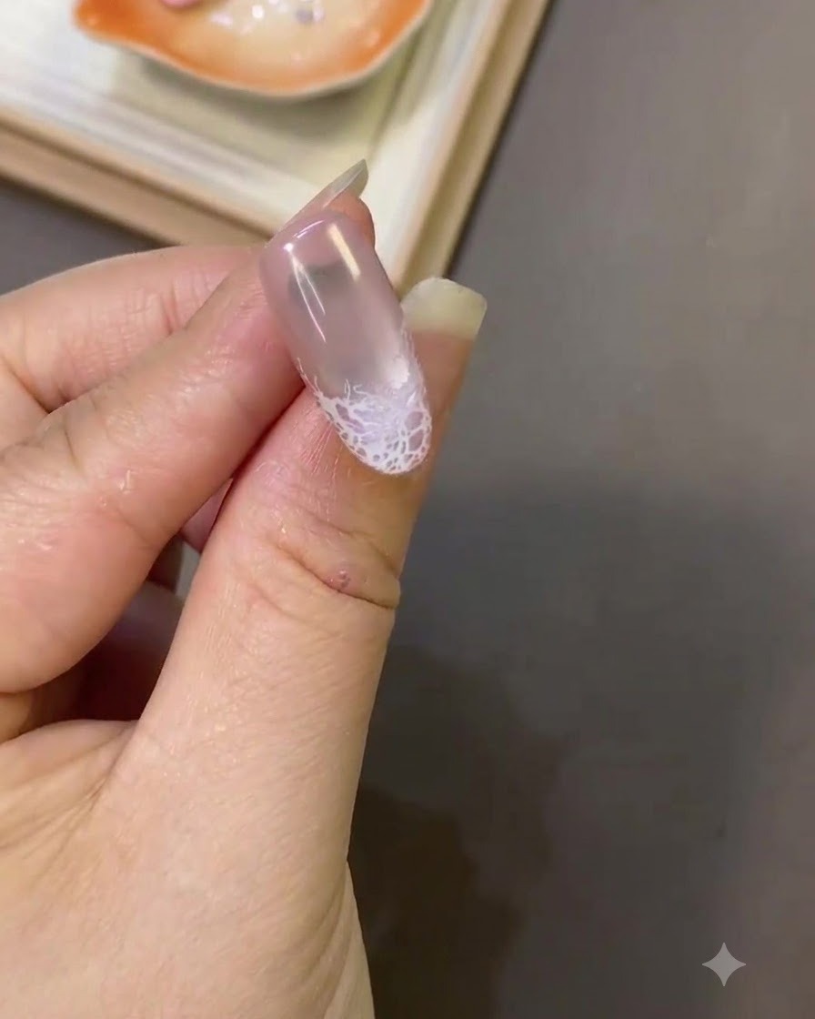 Un primo piano di ununghia che mostra un design in pizzo bianco rifinito vicino alla punta con una consistenza superficiale liscia.