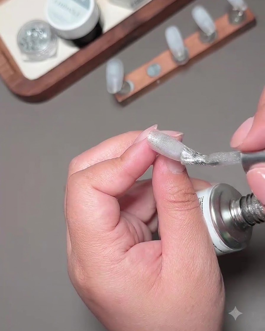 Un pennello che applica lo smalto gel cat-eye con frammenti argentati su una punta per unghie.