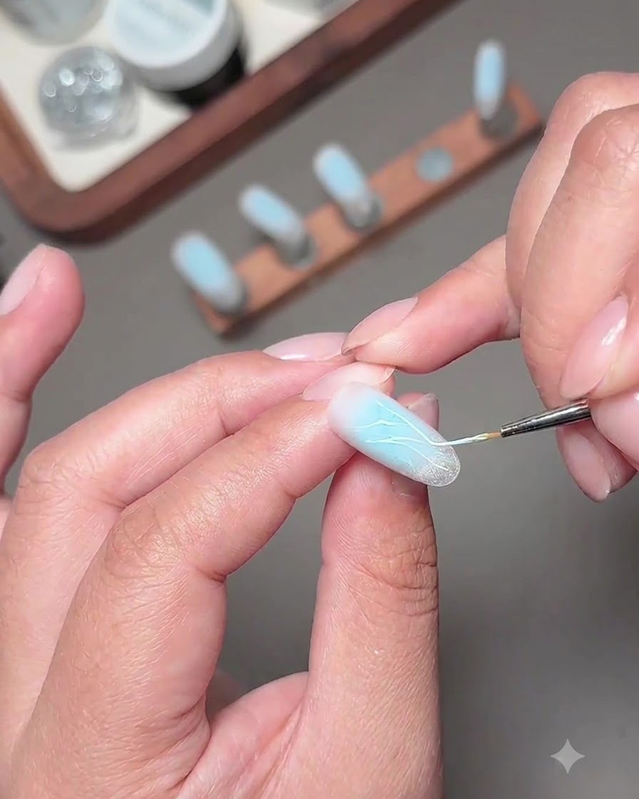 Un pennello fine che applica linee scintillanti di gel diamante frammentato sullunghia decorata.